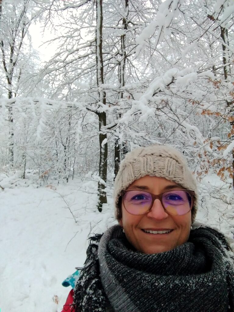 Frau mit dickem Schal und Wintermütze im schneebedeckten Wald