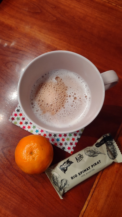 Latte Macchiato Tasse mit einer Mandarine und einem KoRo Bio Spinat Pirat Powerriegel
