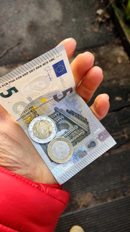 Geöffnete Frauenhand mit einem 5€-Schein, einer 2€- und einer 1€-Münze